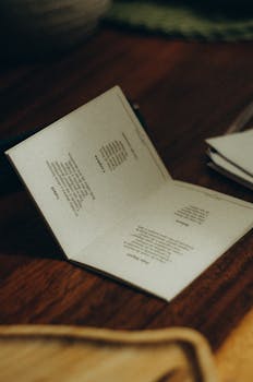 A close-up view of an open book on a wooden table under warm lighting, showcasing printed poetry.